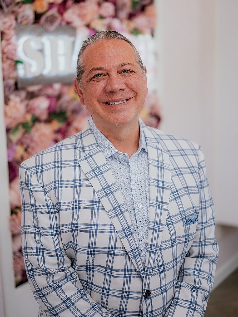 Smiling man in checkered blazer against floral background.