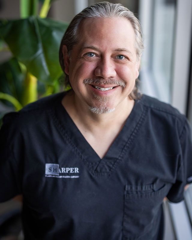 Smiling man in black scrubs, indoors.