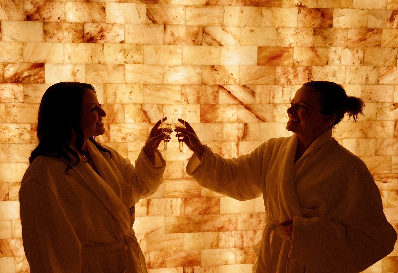 Two women toasting in spa robes.
